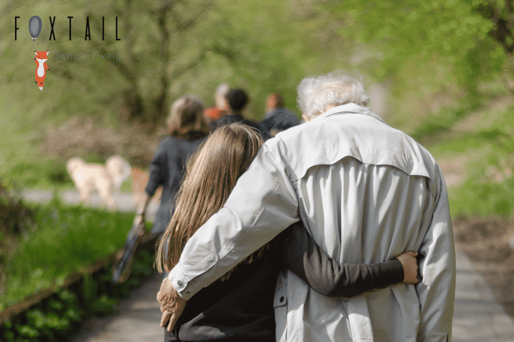 An older man and young woman walking together holding each others waists in a park.