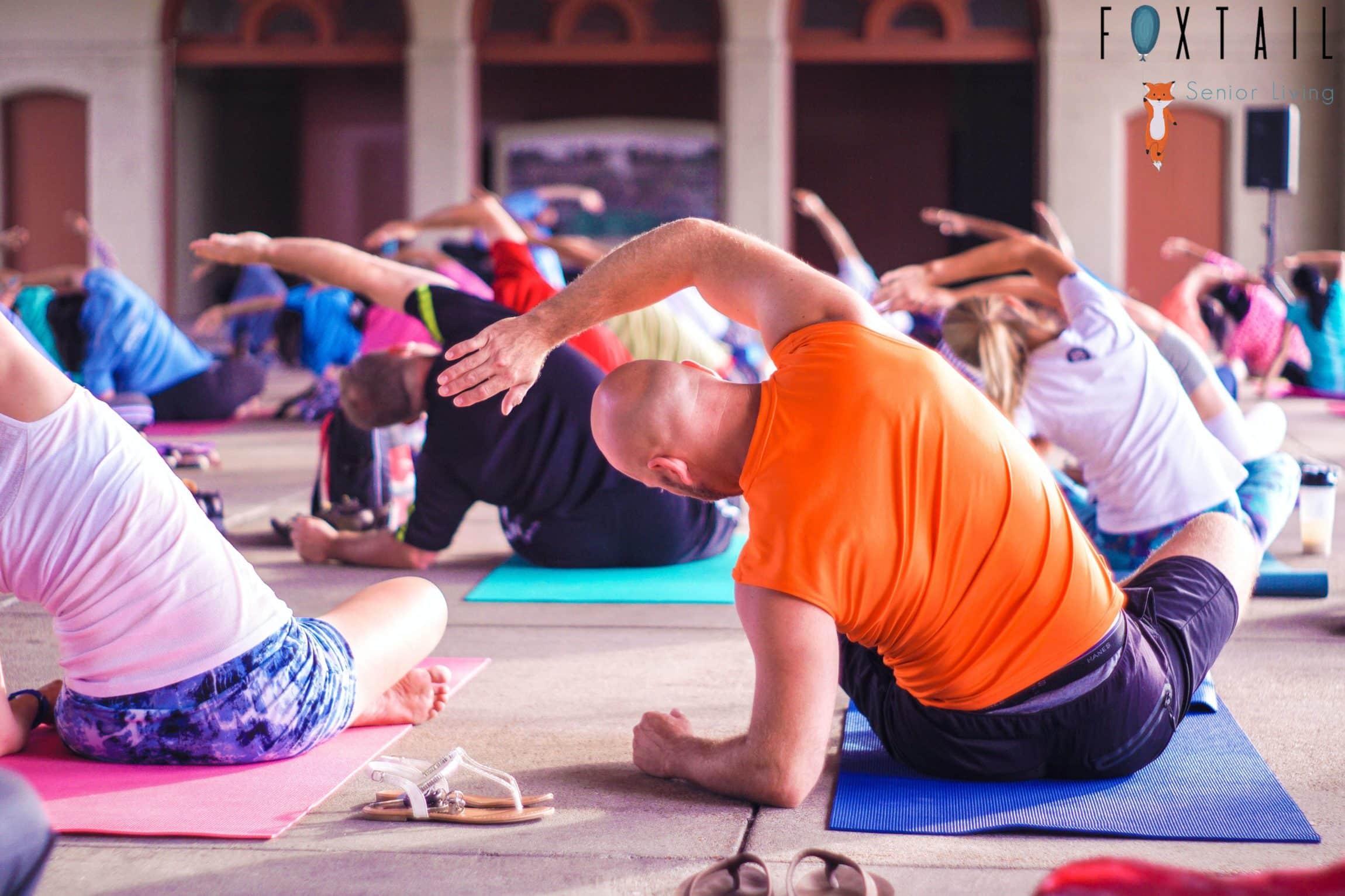 Man in an orange shirt doing a yoga pose in a yoga class.