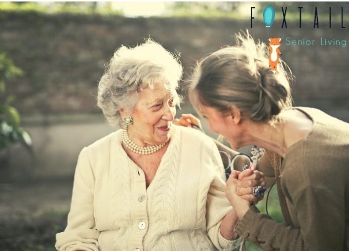 Two older women sitting and laughing together, holding hands.